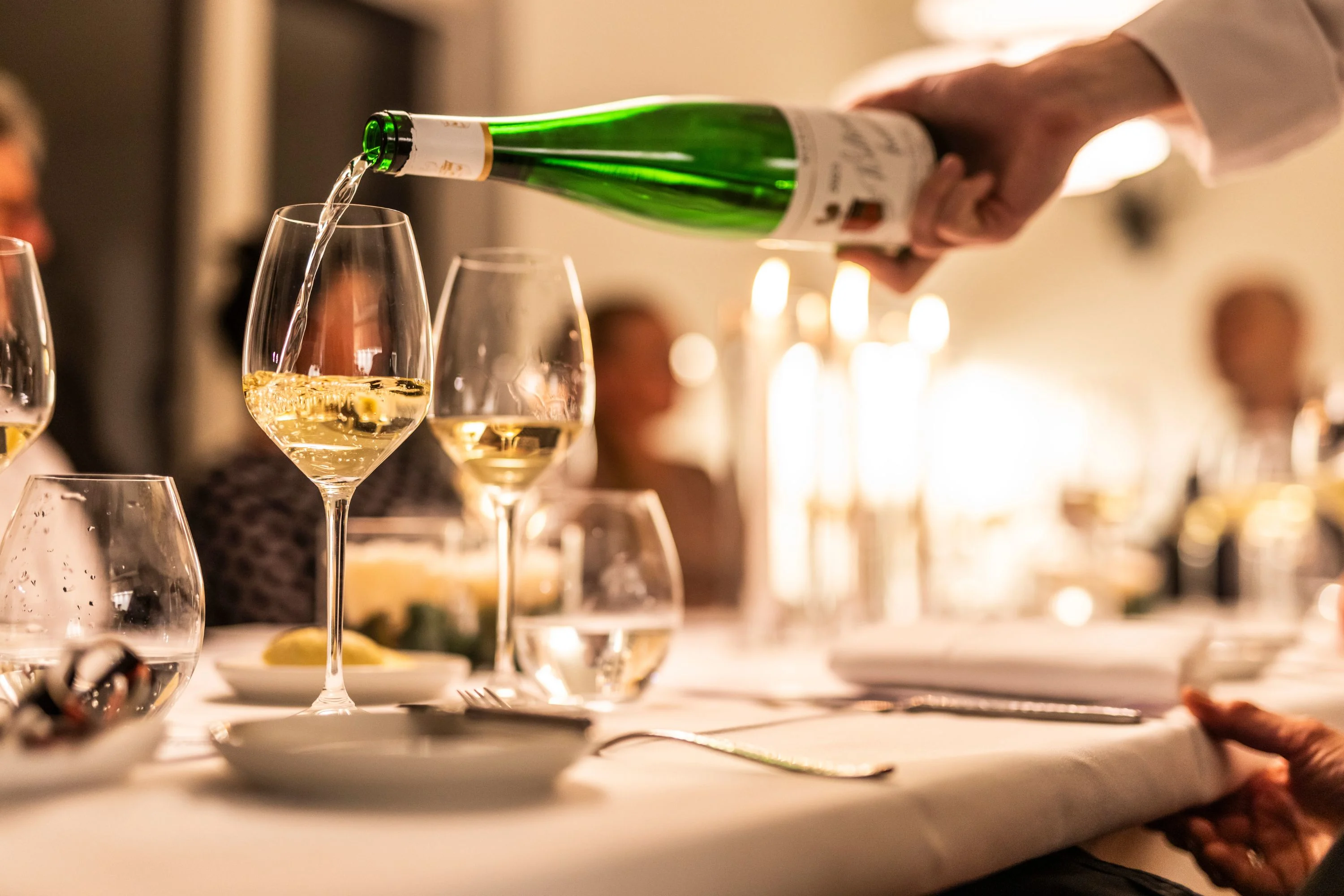 Restaurant-Havlit_Faaborg-Fjord_Hvidvin sænkes op i vinglas, gæster i baggrunden.webp