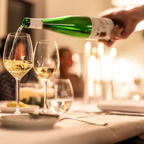 Restaurant-Havlit_Faaborg-Fjord_Hvidvin sænkes op i vinglas, gæster i baggrunden.webp